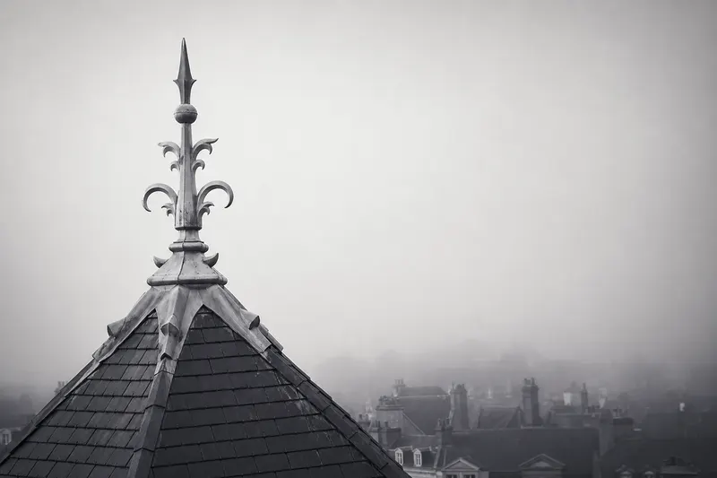 Épi de faîtage en zinc restauré, se détachant sur un ciel de brume
